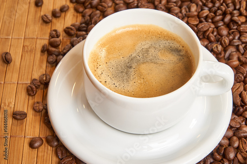 Fresh cup of coffee surrounded by coffee beans on a wooden background