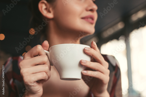 woman holding a cup of coffee in hand, sitting in the morning in a cafe and smiling