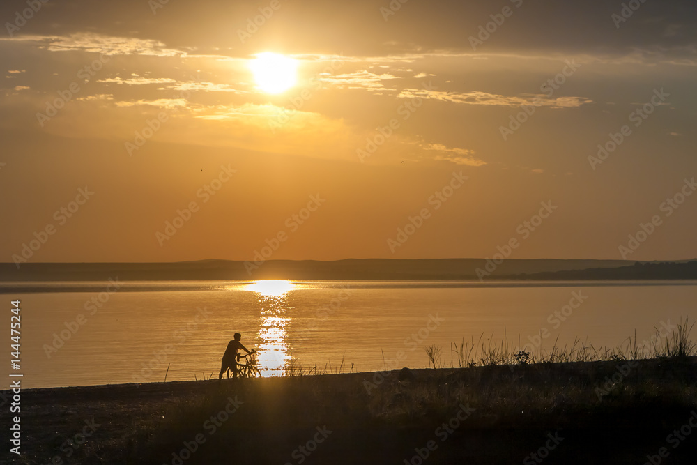 Beautiful colorful summer sea sunrise landscape with a blue sky and unrecognizable man with a bicycle silhouettes walking in the front of the Sun. In Crimea, Azov sea, Ukraine 2013.