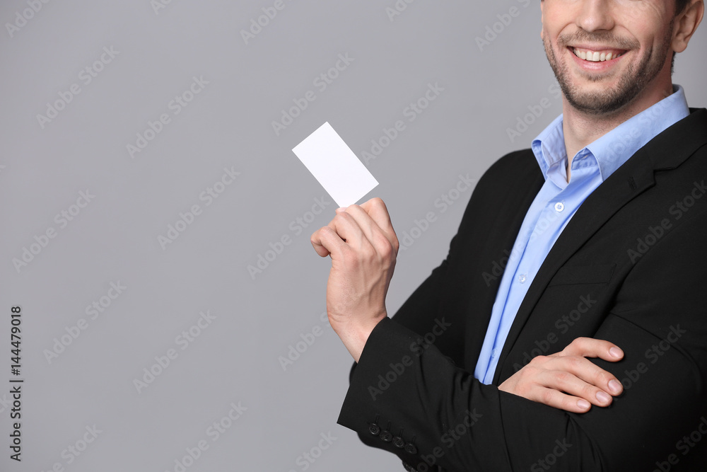 Handsome young man with business card on grey background Handsome young man with business card on grey background