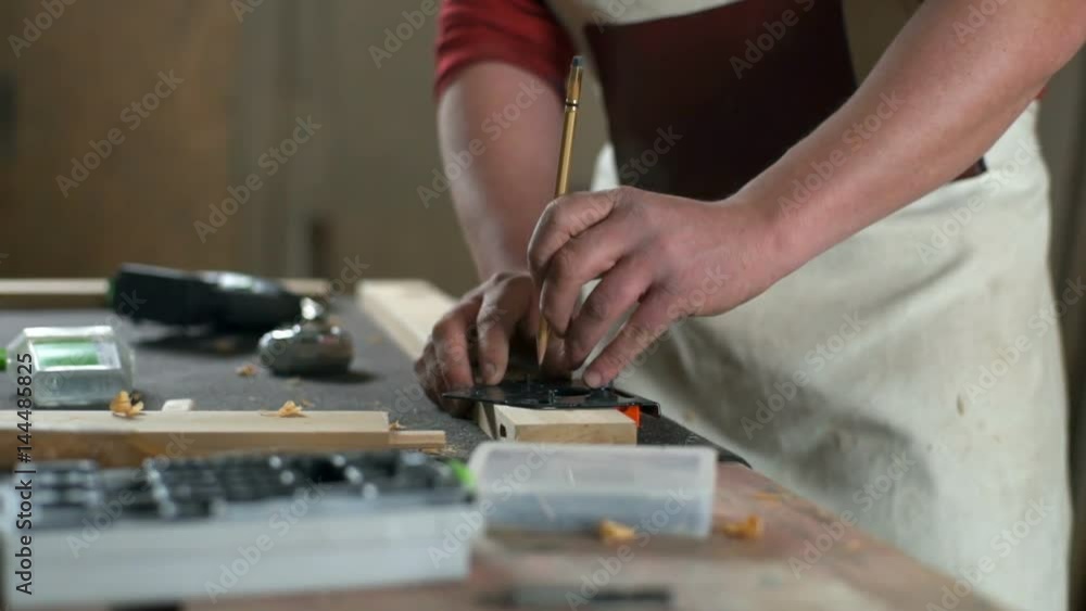 Carpenter leaving marks on a piece of wooden plank with a pencil in a workshop Carpenter leaving marks on a piece of wooden plank with a pencil in a workshop
