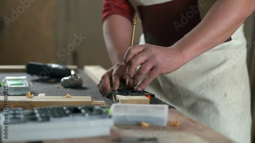 Carpenter leaving marks on a piece of wooden plank with a pencil in a workshop photo