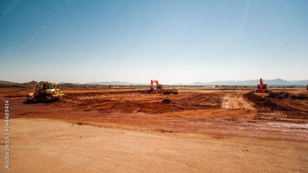 Static pan timelapse of a construction site on a mine while earthworks is in progress with heavy load machinery, trucks and tippers close to action