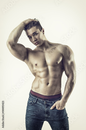 Handsome young muscular man shirtless wearing jeans, on lightbackground in studio shot