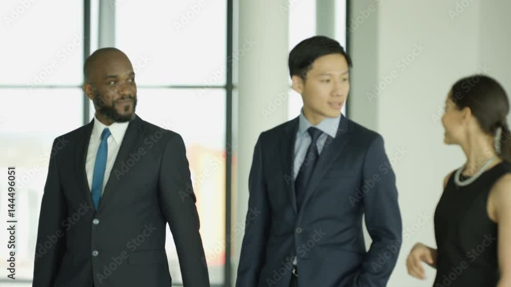 Cheerful business group chatting as they walk through busy modern office Cheerful business group chatting as they walk through busy modern office