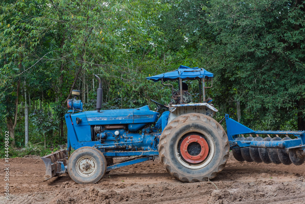 A tractor working in farm with agricultural workers . A tractor working in farm with agricultural workers .