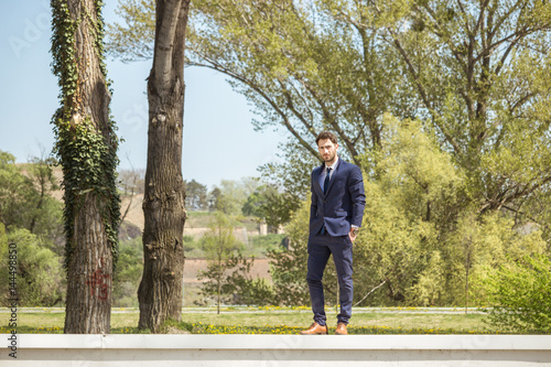 one young man, formal clothes suit shoes, standing on wall, nature outdoors