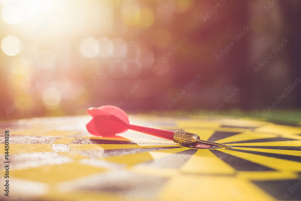 Red dart arrow in the center of dartboard. Blur and bokeh in sunrise time background Red dart arrow in the center of dartboard. Blur and bokeh in sunrise time background