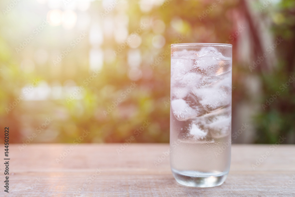 Glass of cold water with ice on table with blur nature garden background Glass of cold water with ice on table with blur nature garden background