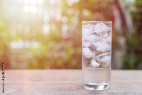 Glass of cold water with ice on table with blur nature garden background