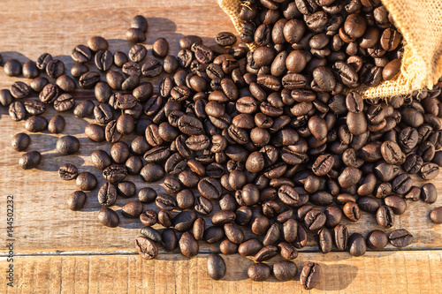 Roasted coffee beans in small sack on wooden table. Outdoor shooting with sunlight and blur background