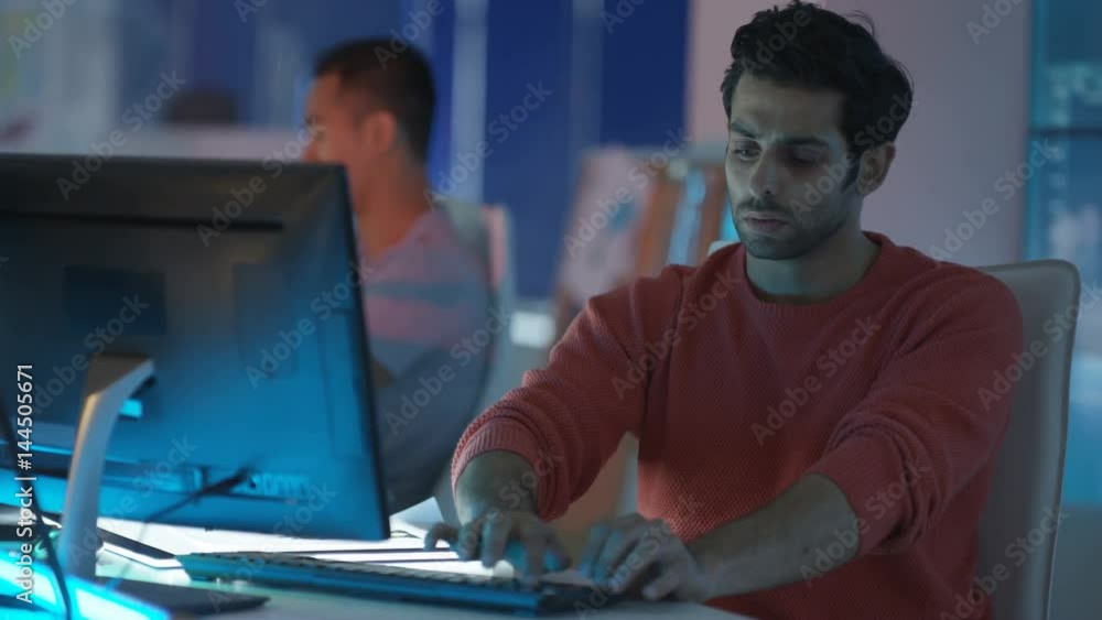 Young creative computer game designer working with colleagues in dark office.