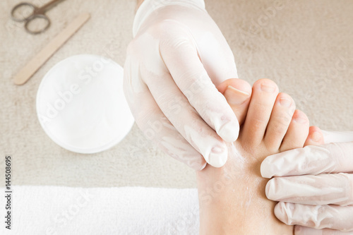Hands in gloves cares foot nails. Pedicure beauty salon. Foot moisturizing cream.