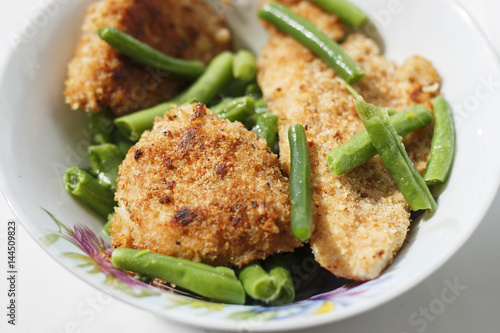chicken in breadcrumbs with green beans and broccoli in a white plate