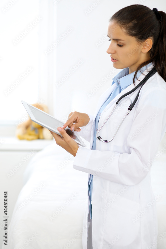 Young brunette female doctor standing and smiling at hospital. Physician ready to examine patient Young brunette female doctor standing and smiling at hospital. Physician ready to examine patient