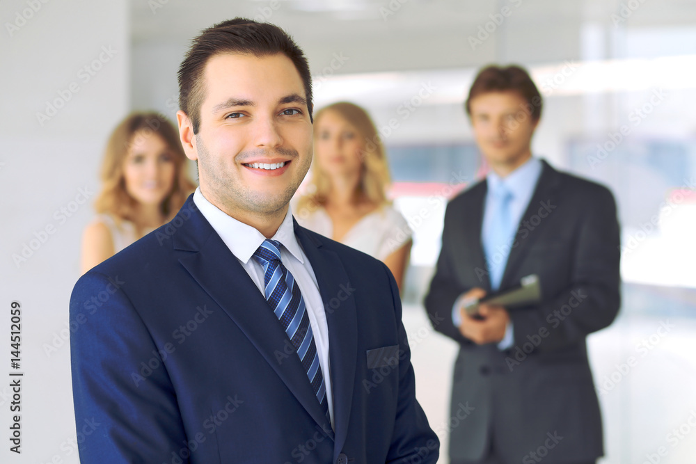 Smiling businessman  in office with colleagues in the background.