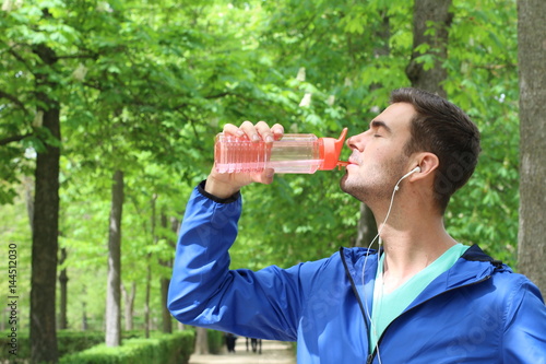 Healthy man drinking water after working out in the park with copy space