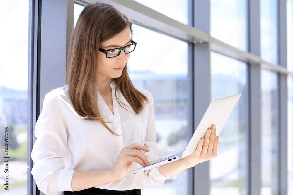 Modern business woman typing on laptop computer while standing in the office before meeting or presentation. Modern business woman typing on laptop computer while standing in the office before meeting or presentation.