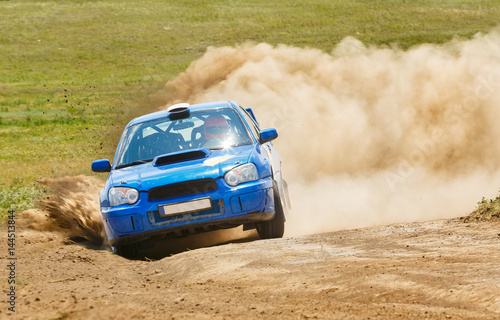 A blue rally car rides along a dusty road