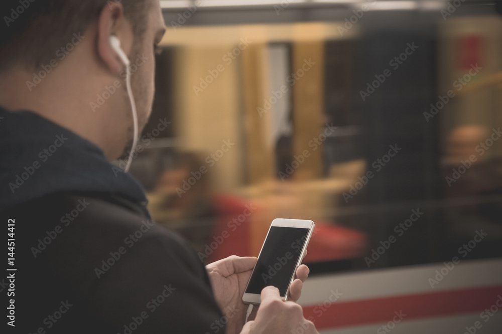 Urban man using smartphone and earphones at the train station 