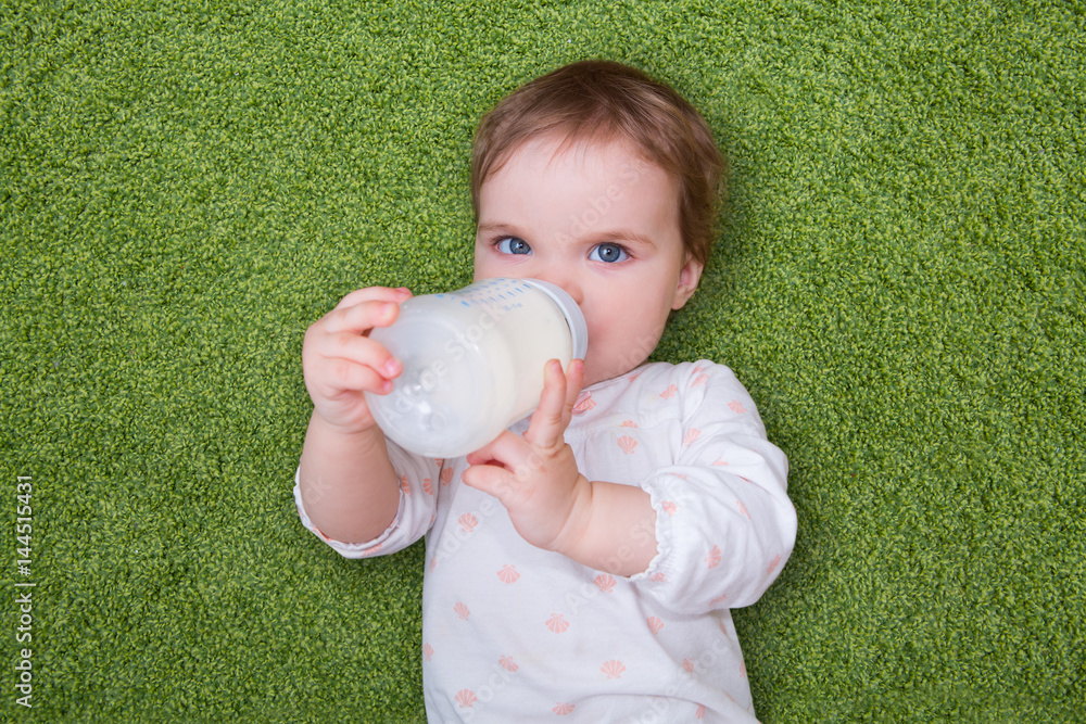 baby drinking milk from bottle lying on a green carpet. Baby holding