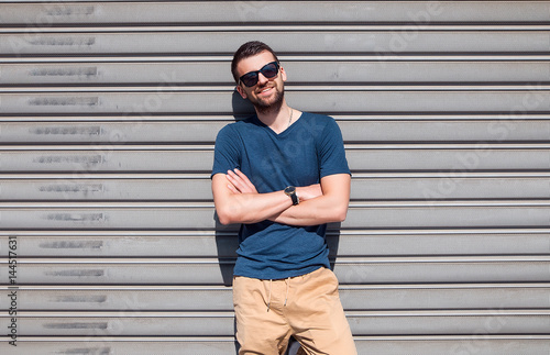 Handsome Man having fun near white wall. Man holding sunglasses near white background.Man in casual clothes.Blue shirt.Bearded man with hand watch.Happy guy.Hipster boy looking to a top.Stylish