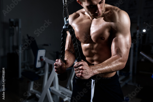 Muscular young man training triceps in the gym photo