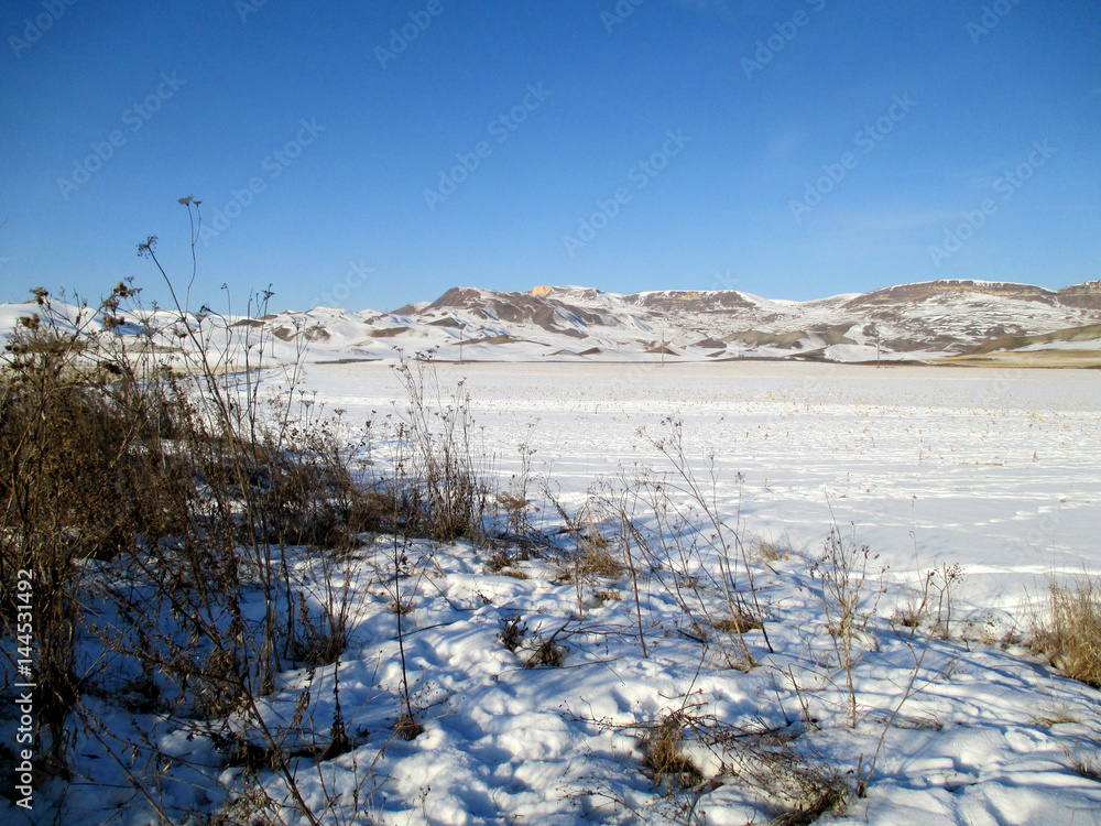 Snow-covered field in sunny winter day on blue sky background, horizontal view. Snow-covered field in sunny winter day on blue sky background, horizontal view.