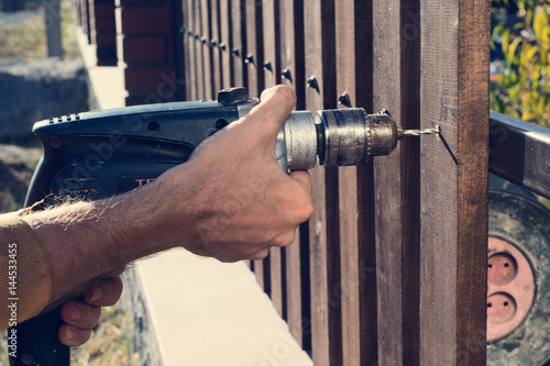 Man hands drilling wooden fence to metal construction. Building a wooden fence with a drill and screw. Close up of his hand and the tool in a DIY concept.