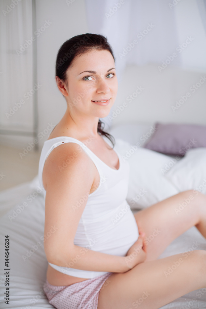 Young pregnant woman is sitting in the bedroom Young pregnant woman is sitting in the bedroom