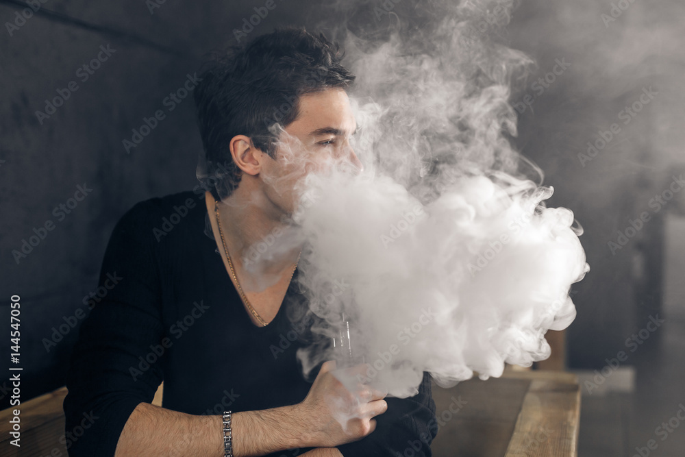 Vaping man holding a mod. A cloud of vapor. Black background. Smoking electronic cigarette Vape advertisement concept