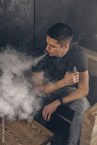 Vaping man holding a mod. A cloud of vapor. Black background. Smoking electronic cigarette Vape advertisement concept
