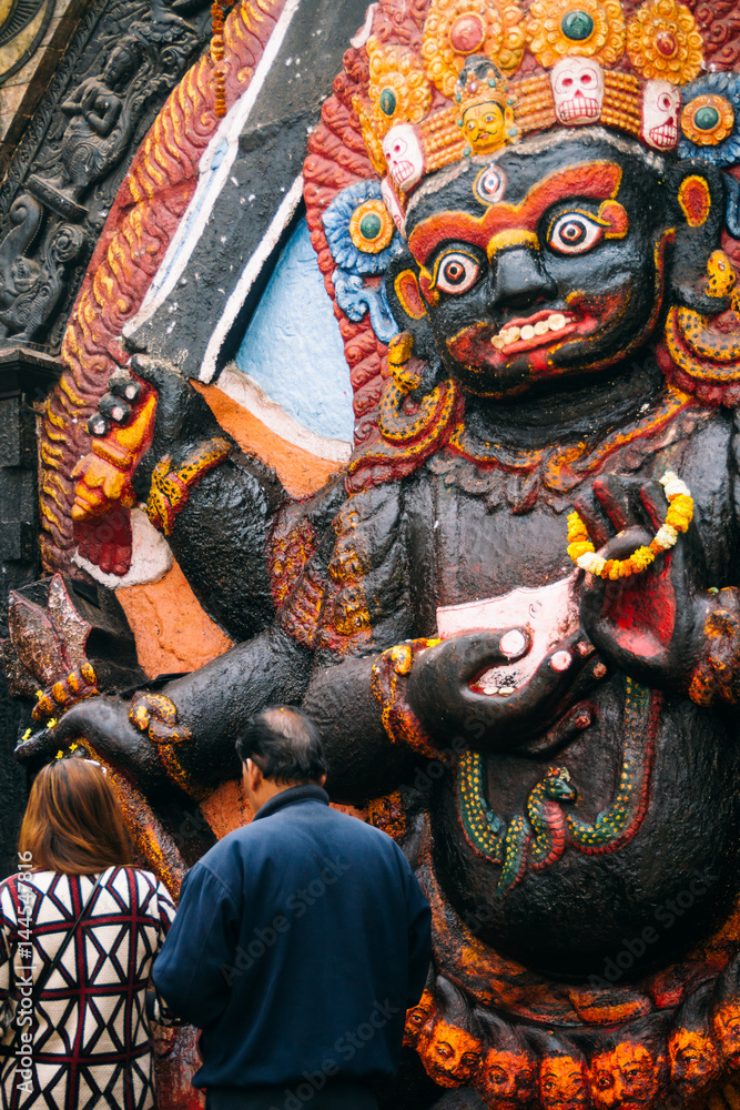 A man and woman place offerings at the foot of this depiction of Kala Bhairav in Durbar Square, Kathmandu.