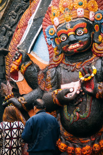 A man and woman place offerings at the foot of this depiction of Kala Bhairav in Durbar Square, Kathmandu.