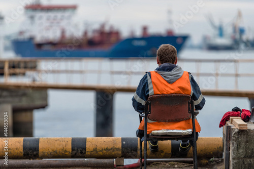 Roustabout leisure time sits on the embankment and looking at ships.