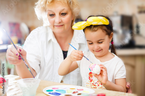 Grandmother with granddaughter are coloring eggs for Easter.