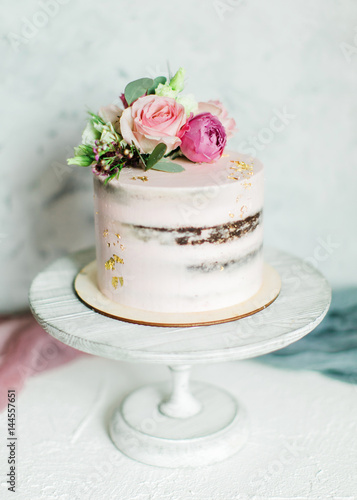 Wedding cake decorated with fresh flowers and gold leaf. On a stand, on a light background