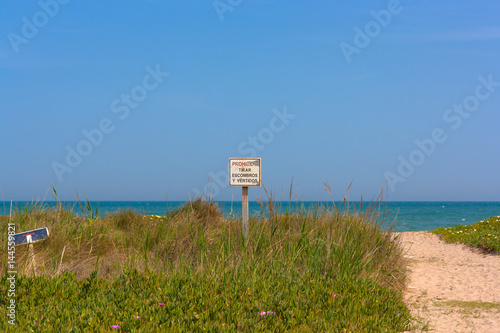 Sign in Spanish forbidding to trow garbage and blooming meadow with beautiful clear blue sky above and sea on the background. photo