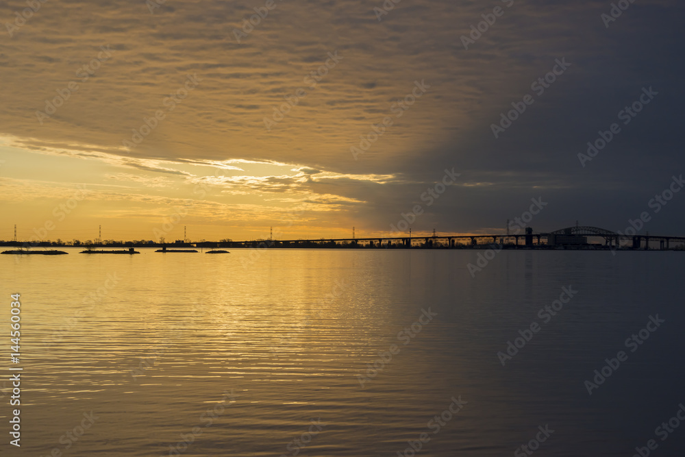 Beautiful sunrise and stormy sky over tranquil lake waters, bridge in silhouette
