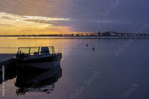 Brilliant golden and violet sunrise over calm waters, recreation boat and birds silhouetted in foreground