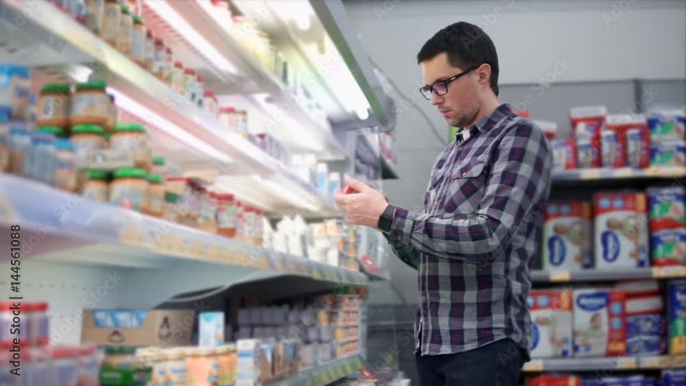 Man in the shopping center choosing goods. Choosing and inspecting the baby food. Rows of shelves with goods and products for children. Concept of shopping in the mall. Man in the shopping center choosing goods. Choosing and inspecting the baby food. Rows of shelves with goods and products for children. Concept of shopping in the mall.