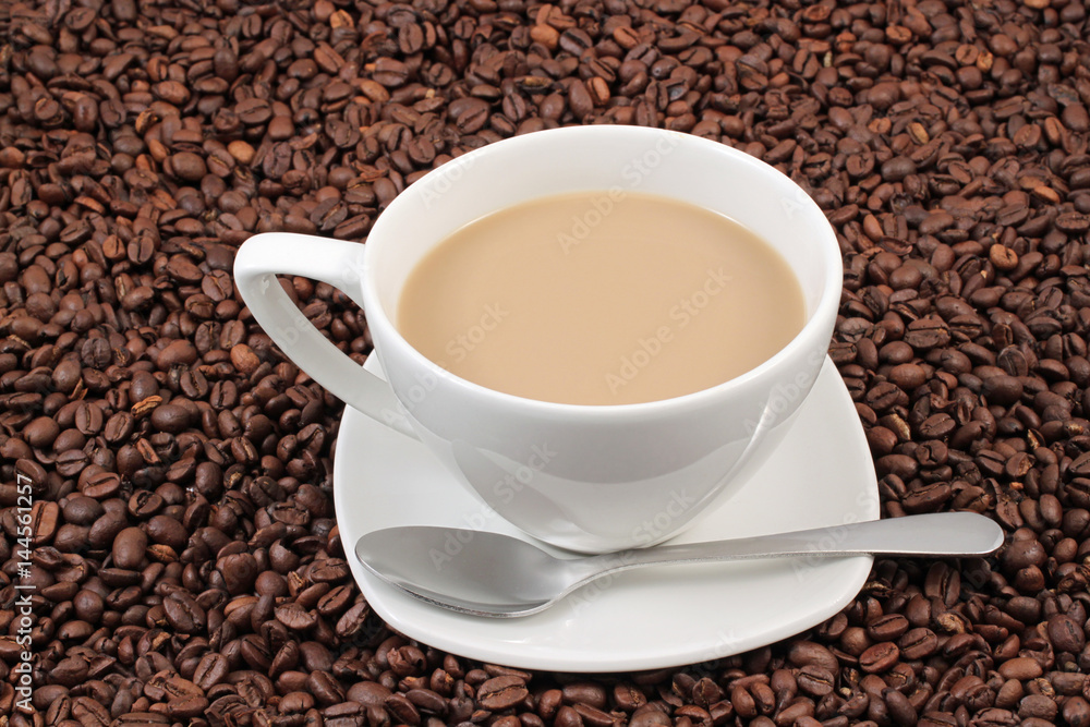 A white coffee cup on a background of whole coffee beans A white coffee cup on a background of whole coffee beans
