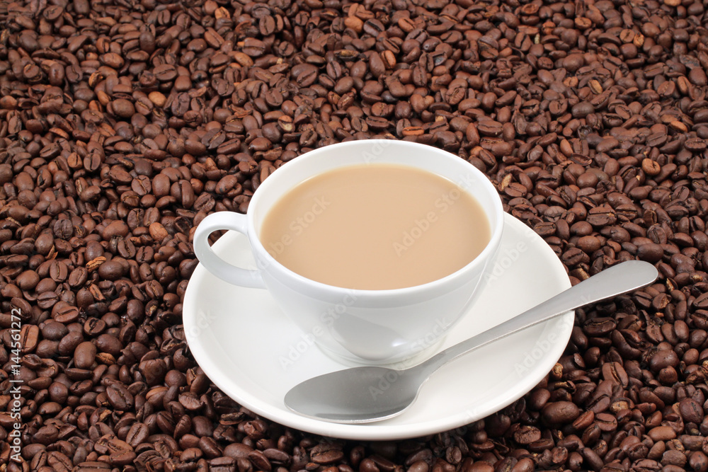 A white coffee cup on a background of whole coffee beans A white coffee cup on a background of whole coffee beans