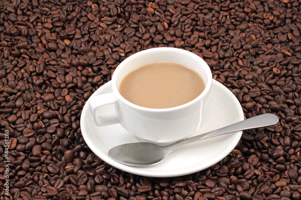 A white coffee cup on a background of whole coffee beans A white coffee cup on a background of whole coffee beans