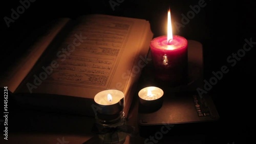Quran with candles, close, dolly shot. Quran is the central religious text of Islam, which Muslims believe to be a revelation from God
