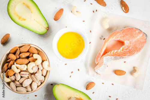Healthy food. Products with healthy fats. Omega 3, omega 6. Ingredients and products: trout (salmon), flaxseed oil, avocado, almonds, cashews, pistachios. On a white stone table. Copy space top view