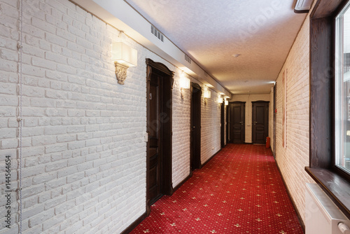Corridor in a hotel with a red carpet, walls of white brick