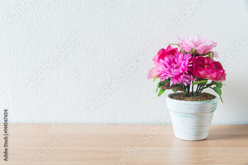 artificial flower pot on wooden table and white wall background