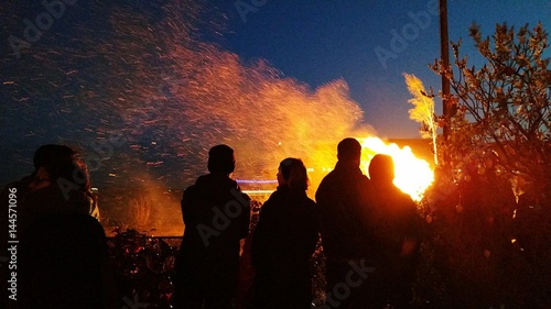 Menschen stehen und beobachten am Abend ein Osterfeuer zur Wintersonnenwende und Austreibung der Geister