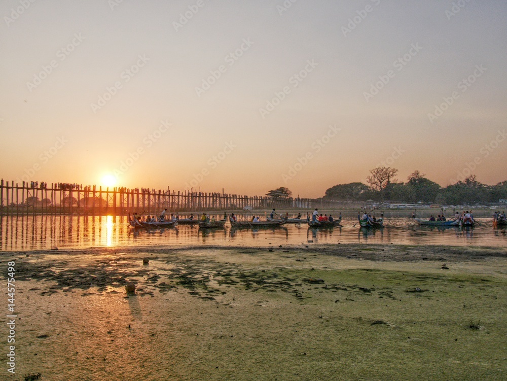 U-bein bridge at sunset with traditional long tail boats in foreground at Mandalay, Myanmar